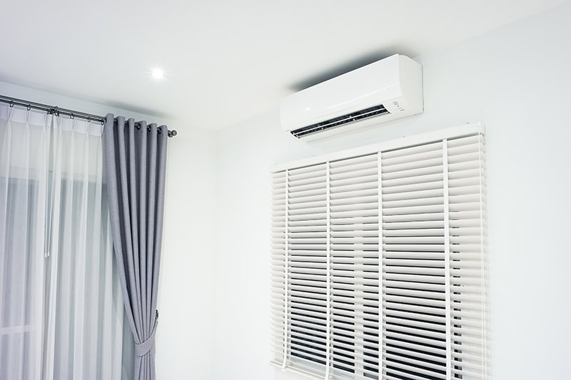 A ductless unit on a wall next to blue curtains.