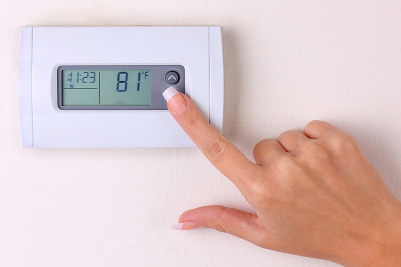 Thermostat 101 Basics. Photo of someone pressing buttons on a digital thermostat mounted on a wall.